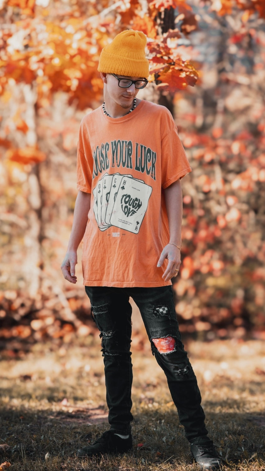 Outdoor autumn style featuring a Tough Love orange 'CHASE YOUR LUCK' tee on a model