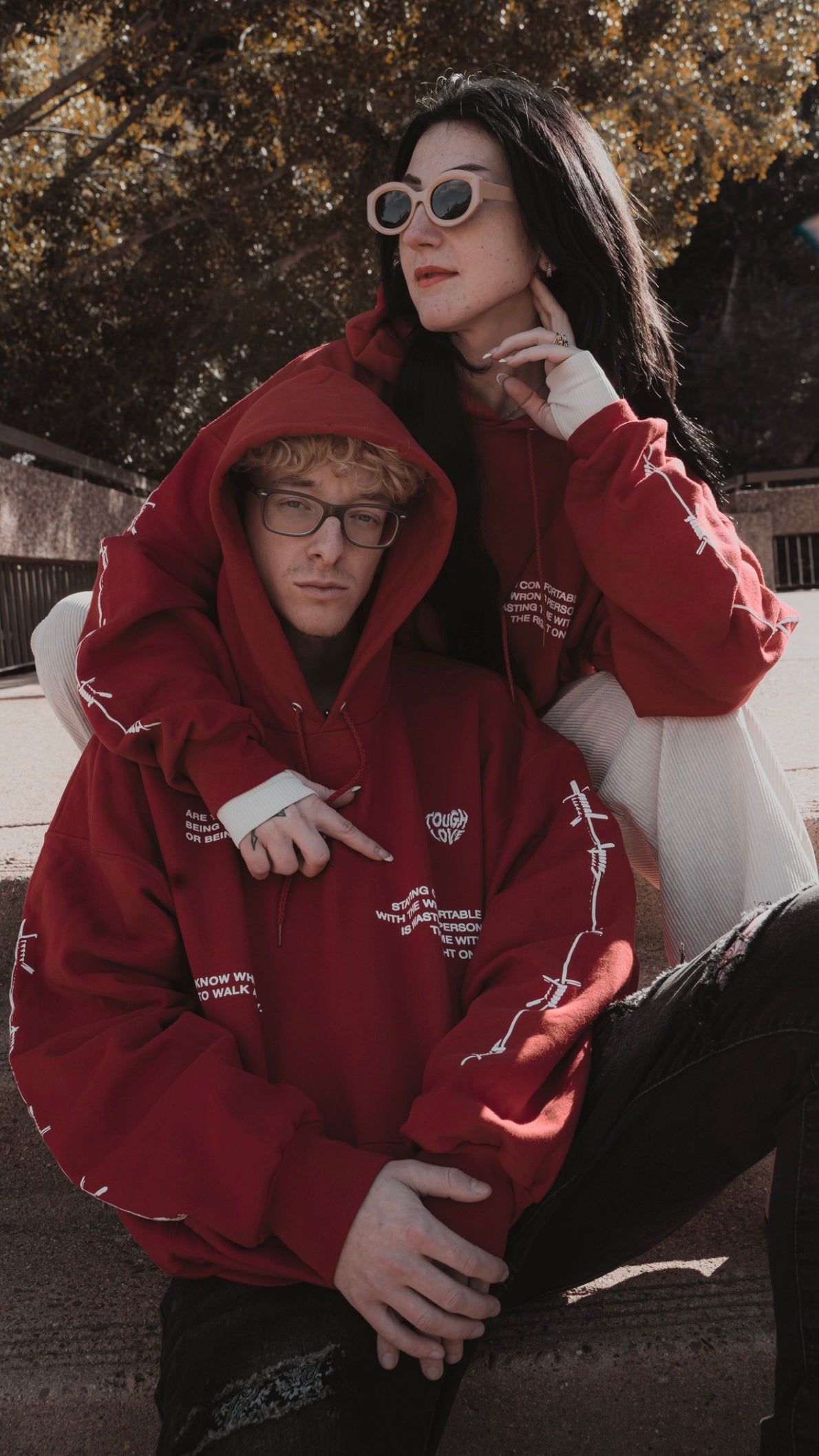 Two models posing in vibrant red Tough Love hoodies with white branding, expressing urban style